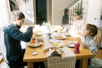 Una familia desayunando juntos en la mesa de comedor de su casa - foto de stock