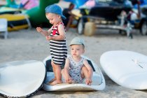 Zwillingsbrüder im Sommer-Outfit spielen im Windsurf-Camp auf einem Brett — Stockfoto