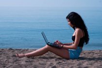 Donna attraente gestisce il suo computer seduto sulla sabbia nella — Foto stock