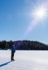 Teenage boy on phone skating on a frozen lake on a sunny winter day. — Stock Photo