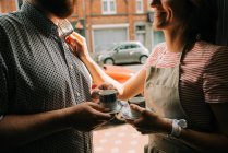 Молодая пара с чашками кофе улыбаются друг другу на улице — стоковое фото