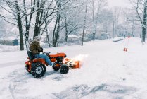Man on a tractor plowing snow in a driveway during a nor'easter storm — Stock Photo