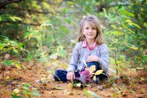 Young blond girl sitting on the ground in the woods. — Stock Photo