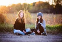 Две красивые молодые девушки, сидящие на улице осенью, с подсветкой. — стоковое фото