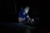 Niño sentado y usando un ordenador portátil, mirando a la pantalla de la computadora - foto de stock
