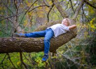 Young blond boy laying on a tree branch quietly. — Stock Photo