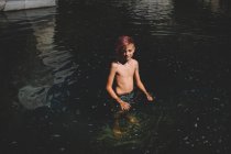 Sourire entre garçon avec des cheveux roses se tient dans un tourbillon d'eau sombre — Photo de stock