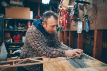 A Caucasian, middle aged man works on a small piece of a wooden airplane in his garage. — Stock Photo