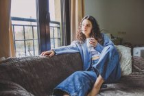Молода жінка снідає на дивані з кавою — стокове фото