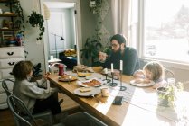 Una familia desayunando juntos en la mesa de comedor de su casa - foto de stock