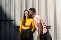 Hombre negro bien parecido moviéndose para besar la cara de una mujer guay mirando a la cámara - foto de stock