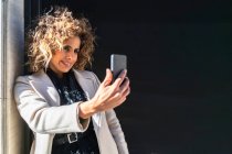 Красива жінка зі смартфоном на чорній стіні — стокове фото