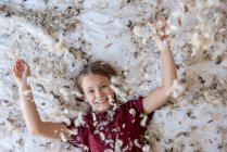 Young blond girl laying on the bed during a feather pillow fight. — Stock Photo
