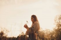 Молодая женщина держит цветок, стоя на поле летом — стоковое фото