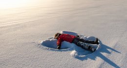 Enfant faisant un ange de neige dans un champ neigeux ouvert au soleil du matin. — Photo de stock
