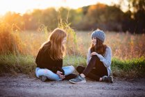 Dos hermosas chicas adolescentes en suéteres sentados fuera en otoño. - foto de stock
