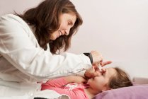 Female doctor smiling and giving eye drops to a little girl in her bed. Home doctor concept — Stock Photo