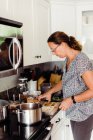 Жінка середнього віку з хвостом поні готує сімейну вечерю на плиті — стокове фото