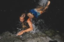 Garçon dans des troncs lumineux Baignades et éclaboussures dans une piscine sombre — Photo de stock