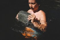 Boy sfonda la superficie dell'acqua con grande pietra — Foto stock