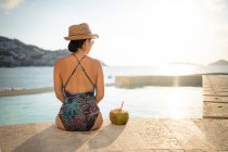 Счастливая женщина отдыхает в бассейне и пьет кокосовую воду — стоковое фото