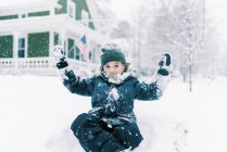 Niño sentado en el banco de nieve en frente de su casa en su patio - foto de stock