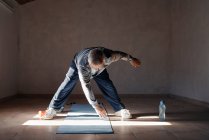Uomo anziano che fa esercizi di stretching e di allenamento con i pesi a casa — Foto stock
