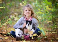 Young blond girl sitting in the woods with black and white cat in lap. — Stock Photo