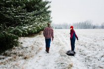 Dois adolescentes caminhando por um campo nevado com pinhos em Michigan — Fotografia de Stock