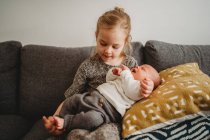 Belle fille blanche tenant le petit frère nouveau-né sur le canapé à la maison — Photo de stock