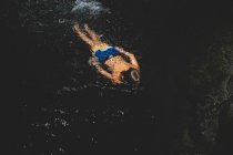 Ragazzo in Bright Trunks Nuota e schizza in una piscina buia — Foto stock