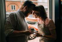 Jovem casal apaixonado bebendo café, sorrindo enquanto está à porta — Fotografia de Stock