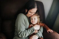 Bela jovem mãe e sua filha no sofá — Fotografia de Stock