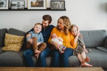 Belle famille blanche heureuse tenant bébé nouveau-né sur le canapé à la maison — Photo de stock