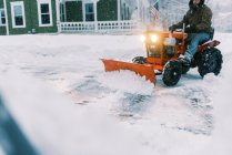Mann auf Traktor pflügt während eines Ostersturms Schnee in einer Einfahrt — Stockfoto