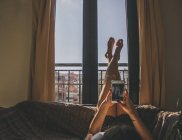 Молодая женщина лежит на диване с поднятыми ногами и фотографирует — стоковое фото