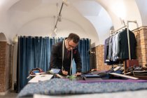 Focused senior male tailor creating sketches on table while working in loft studio — Stock Photo