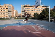 African American player jumping and throwing ball in hoop on basketball court — Fotografia de Stock