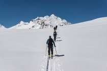 Vue arrière des mâles et des femelles avec des splitboards marchant sur la montagne enneigée contre un ciel dégagé — Photo de stock