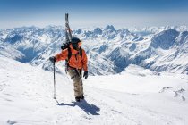 Man with ski pole carrying splitboard while climbing snowcapped mountain during vacation — Stock Photo