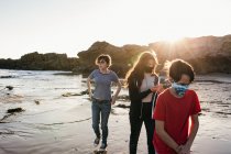 Three Siblings Walk On The Beach At Sunset While Wearing Face Masks — Stock Photo