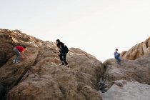 Tres hermanos suben a la cima de una enorme formación rocosa en la playa - foto de stock
