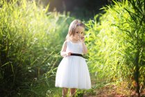 Cute little girl toddler in white dress smelling a daisy in the grass. — Stock Photo