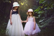 Дві милі маленькі дівчата в пасхальних сукнях тримають руки в лісі . — стокове фото