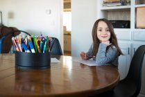 Маленькая девочка сидит за столом с бумагой и карандашом. — стоковое фото