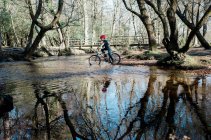 Молодий хлопчик їде по річці, щоб перетнути гірський велосипед — стокове фото