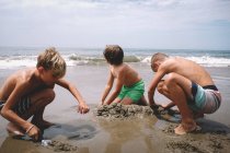 Niños cavan en la arena en un soleado día de verano - foto de stock