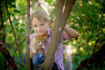 Little blond boy in a tree with a kitten in the country. — Stock Photo