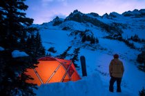 Молодой мужчина стоит снаружи палатки в сумерках зимой — стоковое фото