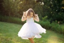 Симпатична маленька дівчинка в білій сукні танцює і крутиться на лузі . — стокове фото